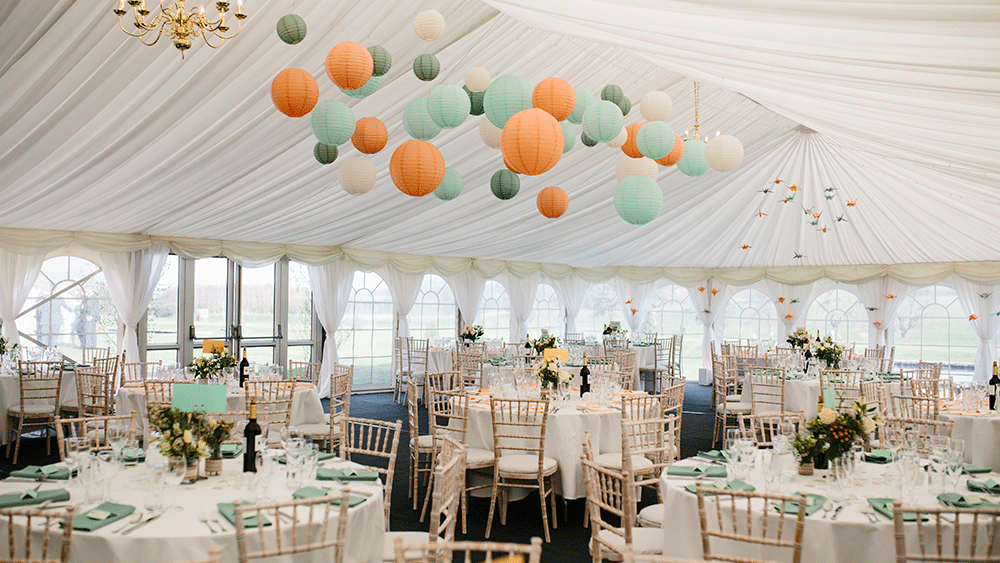 Complementary coloured paper lanterns warm up a white wedding marquee