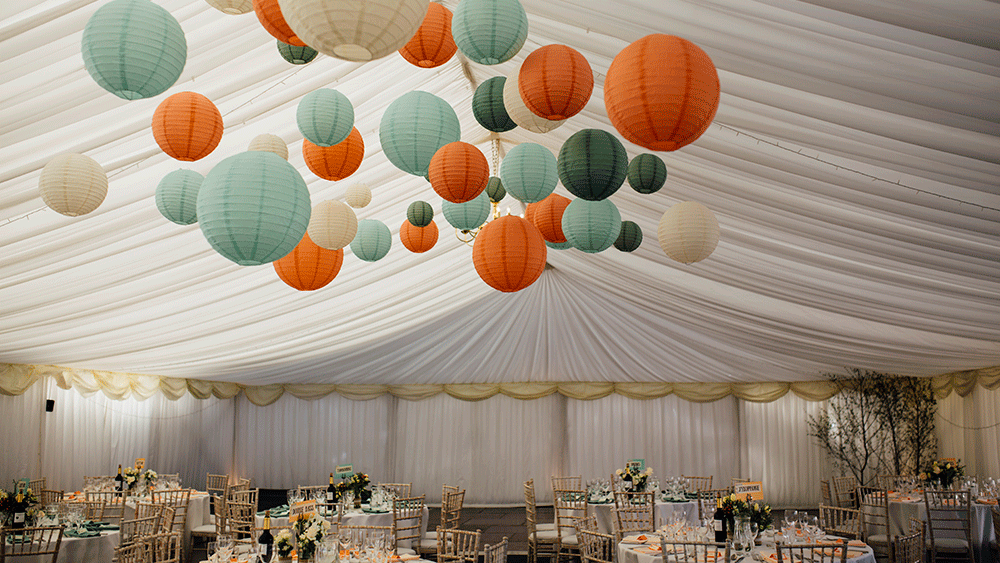 Complementary coloured paper lanterns warm up a white wedding marquee